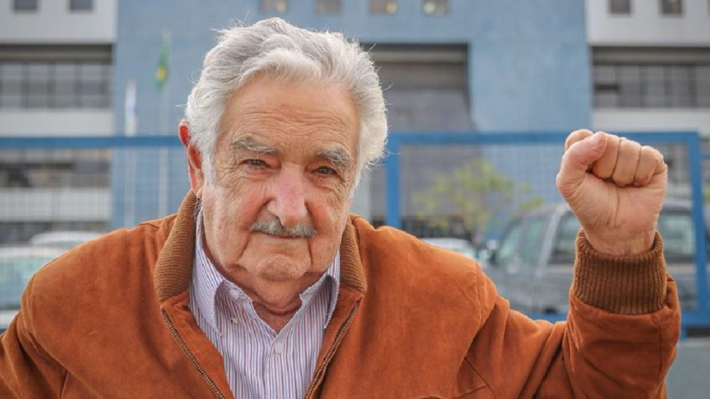 José "Pepe" Mujica acenando, com casaco coral e expressão serena