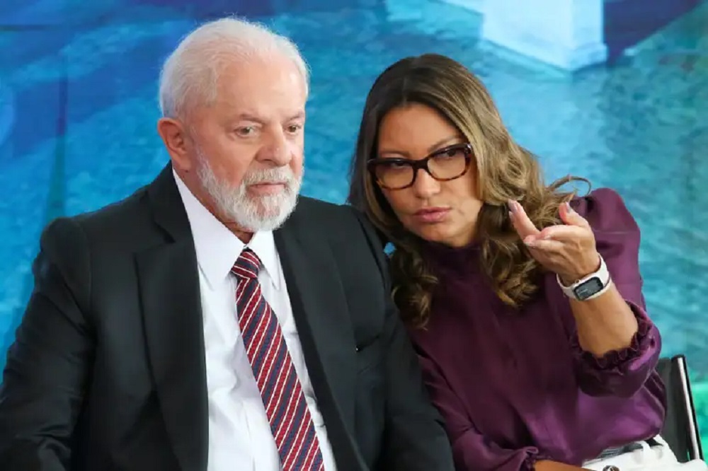 Lula e Janja conversando, sérios, sem olhar para a câmera