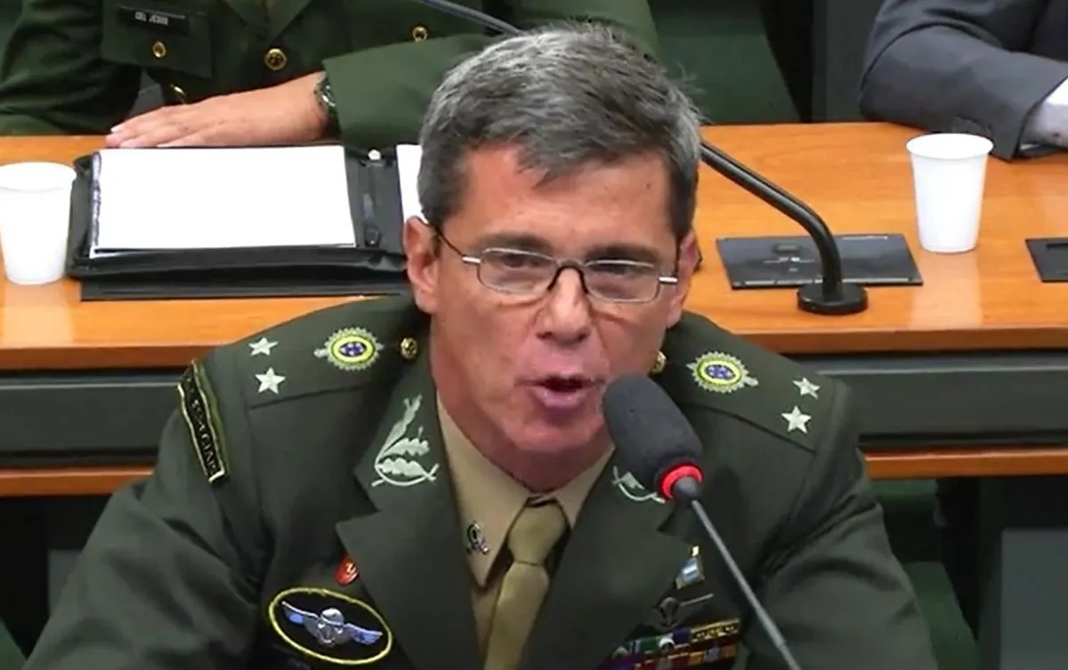 general da reserva Mario Fernandes fardado, falando em microfone, de óculos, sério