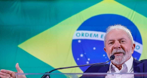 presidente Luiz Inácio Lula da Silva falando e gesticulando com braços abertos e bandeira do Brasil ao fundo