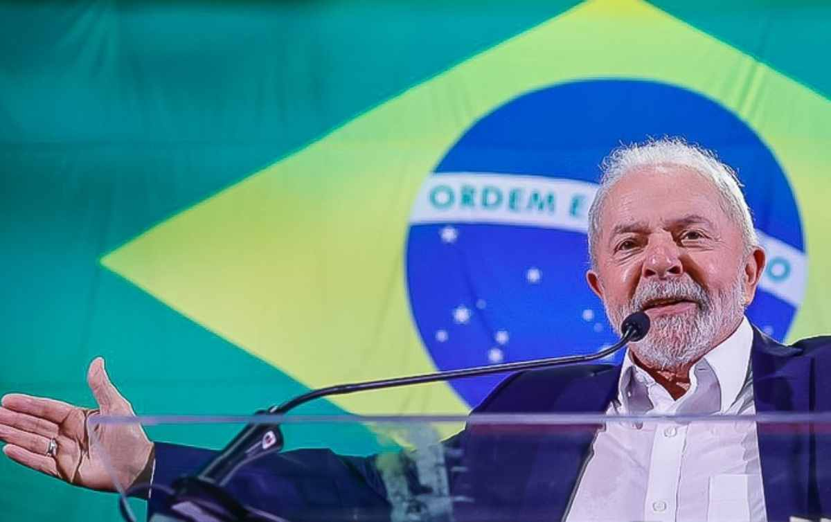 presidente Luiz Inácio Lula da Silva falando e gesticulando com braços abertos e bandeira do Brasil ao fundo