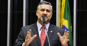 Paulo Pimenta, Ministro-Chefe da Secom do Governo Lula, falando e gesticulando na Câmara, sério, com bandeiras ao fundo