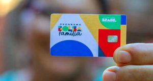 Mulher segurando cartão do Bolsa Família, ela desfocada e o cartão focado na frente
