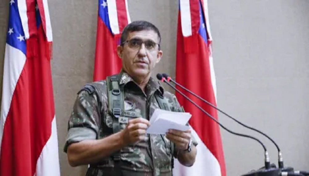 Estevam Theophilo Gaspar de Oliveira, ex-integrante do Alto Comando do Exército, falando em microfone e lendo papel, em pé, perto de bandeiras