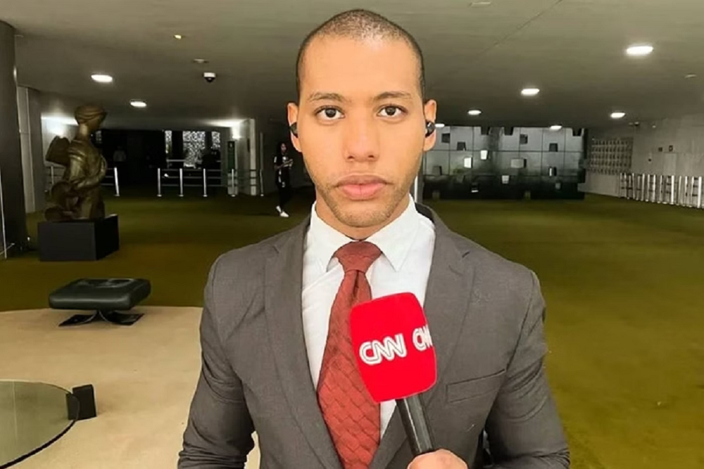 O repórter Izaías Godinho sério, segurando microfone da CNN e olhando pra frente