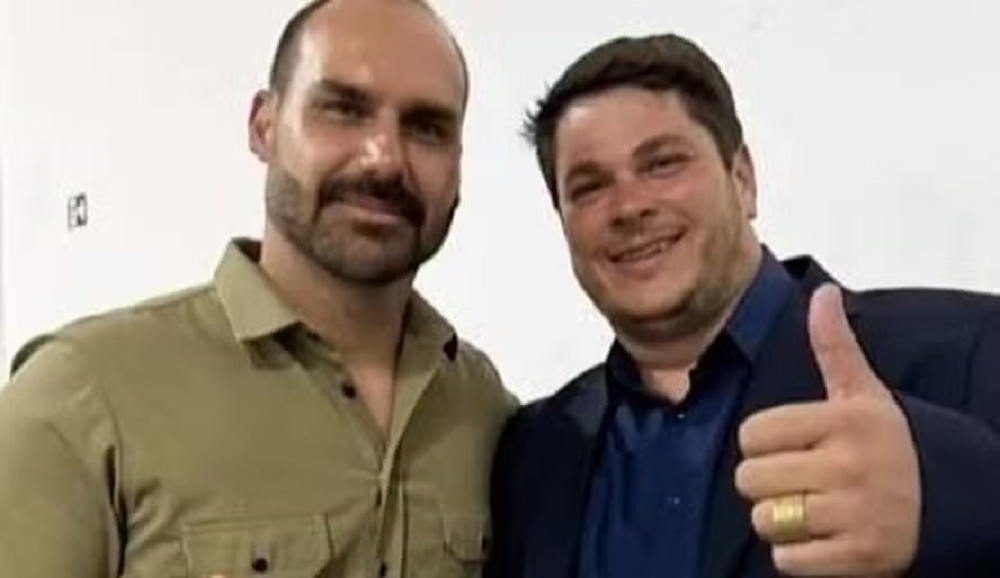O deputado federal Eduardo Bolsonaro (PL) junto a Osvaldo Cabal, ambos sorrindo lado a lado, o segundo fazendo sinal de joia