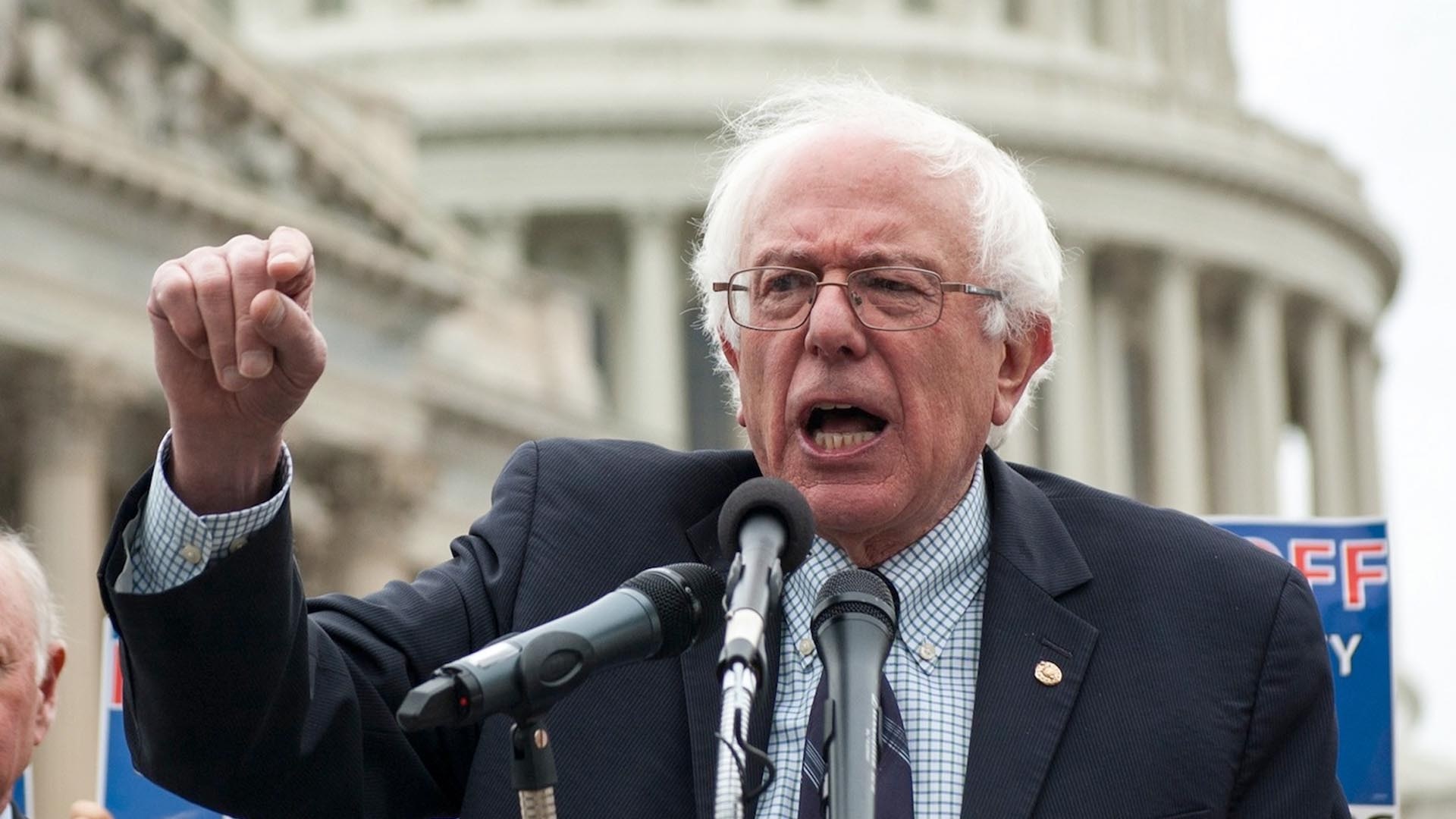 O senador Bernie Sanders falando e gesticulando, sério