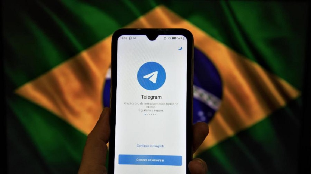 Celular com logo do Telegram e bandeira do Brasil ao fundo