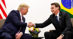 Donald Trump, presidente eleito dos Estados Unidos, e o ex-presidente do Brasil, Jair Bolsonaro, sentados, se olhando em aperto de mãos