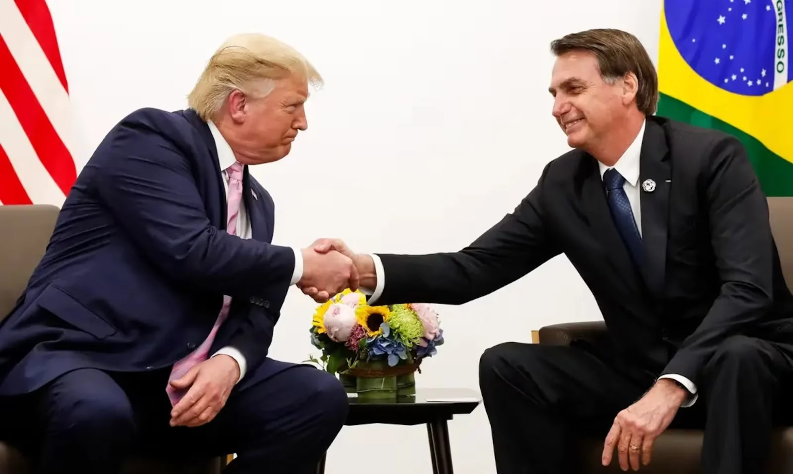 Donald Trump, presidente eleito dos Estados Unidos, e o ex-presidente do Brasil, Jair Bolsonaro, sentados, se olhando em aperto de mãos