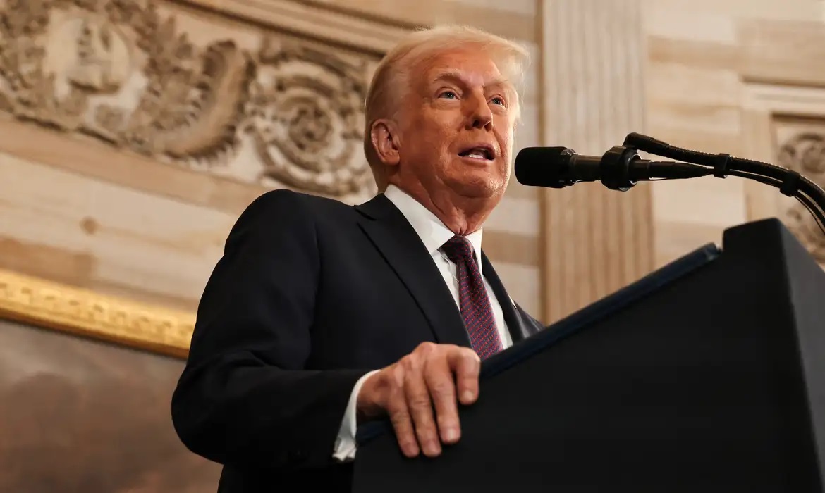 O presidente dos Estados Unidos, Donald Trump, falando em microfone, sério, em foto feita de baixo