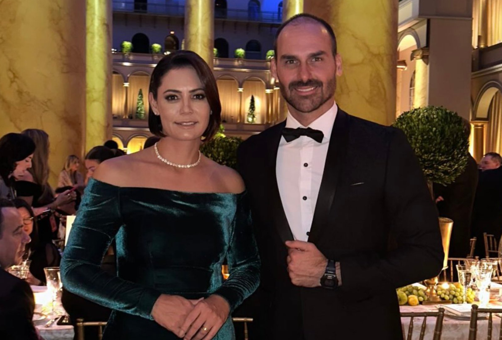 A ex-primeira-dama Michelle Bolsonaro (PL) e o deputado federal Eduardo Bolsonaro (PL) posando sorrindo para foto, em pé, lado a lado