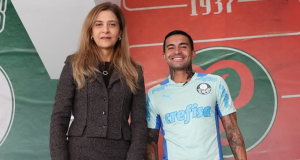 Leila Pereira e Dudu lado a lado, em pé, olhando para a câmera, ela séria e ele sorrindo