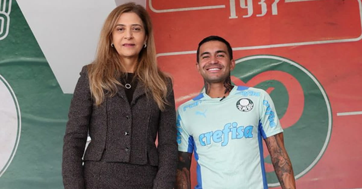 Leila Pereira e Dudu lado a lado, em pé, olhando para a câmera, ela séria e ele sorrindo