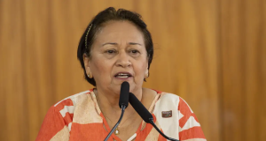 A governadora do Rio Grande do Norte, Fátima Bezerra (PT), falando em microfones, séria, de roupa estampada