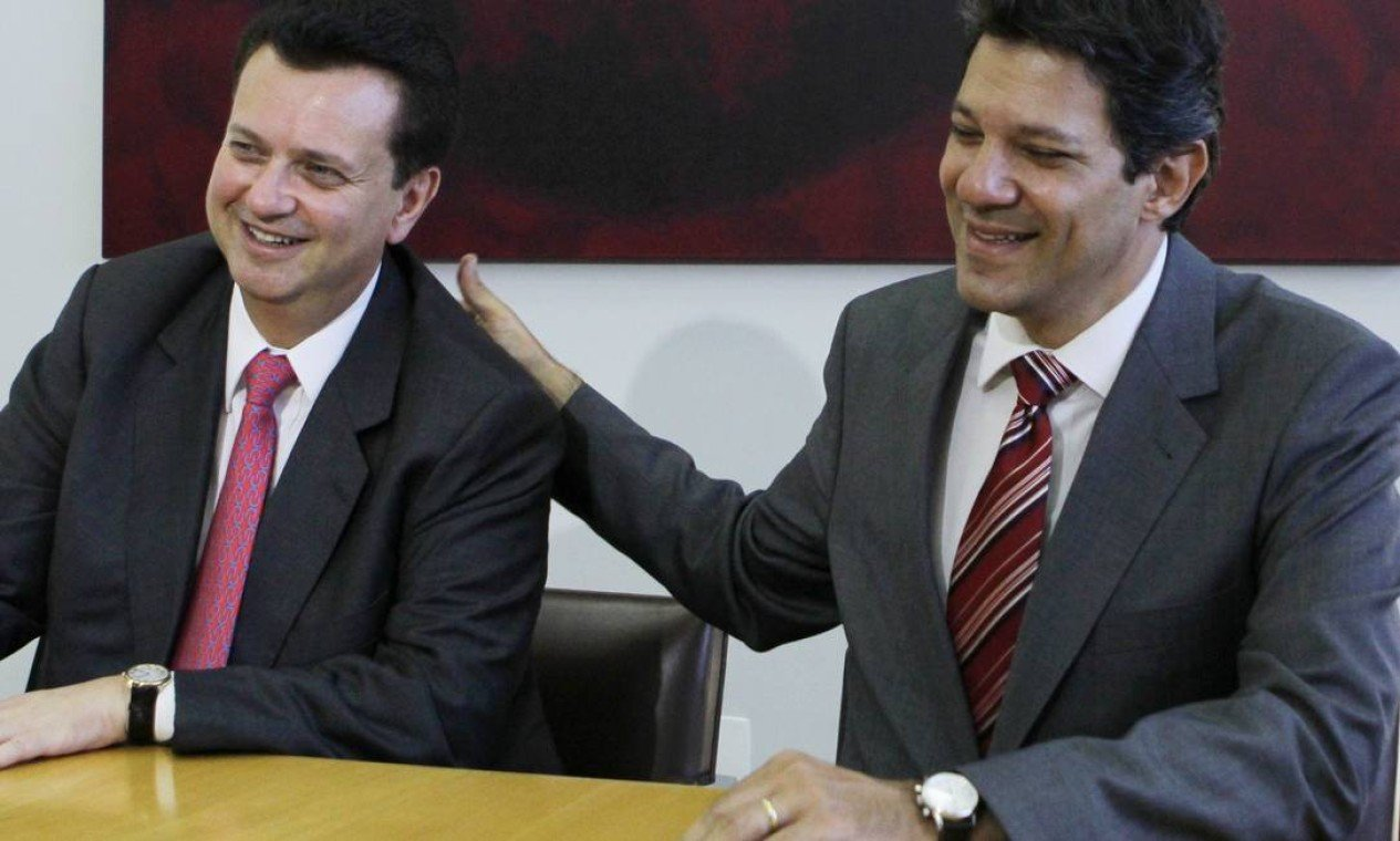 O presidente do PSD, Gilberto Kassab, e o ministro da Fazenda, Fernando Haddad, em foto antiga, sentados lado a lado, sorrindo sem olhar para a câmera
