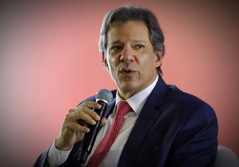 O ministro da Fazenda, Fernando Haddad, falando em microfone, sério, sem olhar para a câmera
