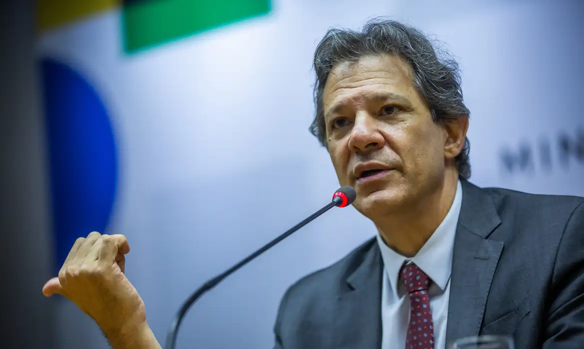 O ministro da Fazenda, Fernando Haddad, falando em microfone e apontando para o lado