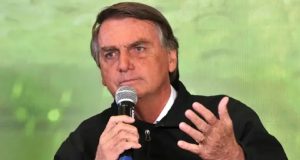 Jair Bolsonaro (PL) falando em microfone e gesticulando, de roupa preta e expressão séria, sem olhar para a câmera