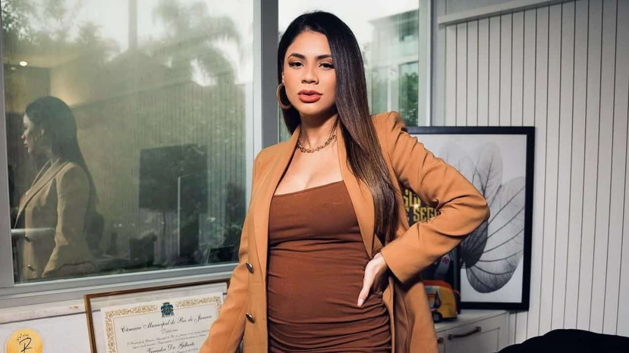 A cantora Lexa de roupa marrom, posando séria, de cabelo solto e mão na cintura