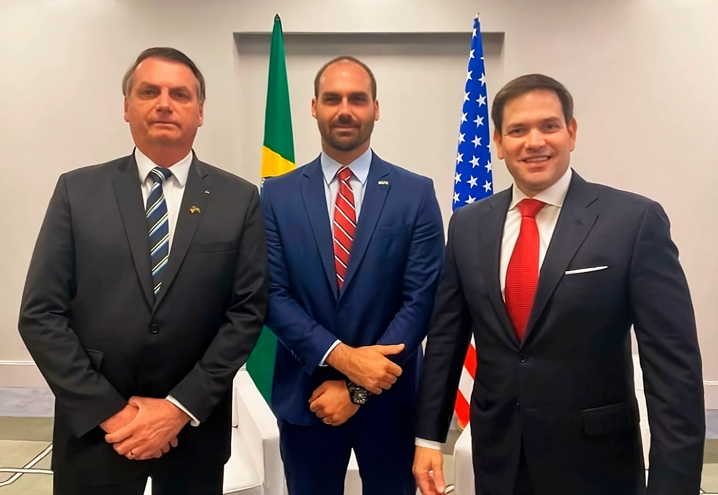 Jair Bolsonaro, Eduardo Bolsonaro e Marco Rubio em pé, lado a lado, posando para foto, o terceiro sorrindo