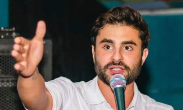 O vereador Pedro Rousseff (PT) de roupa branca, falando em microfone e apontando pra frente