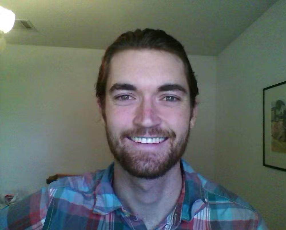 Ross Ulbricht, criador do site Silk Road, sorrindo para a câmera, em local fechado, de roupa xadrez