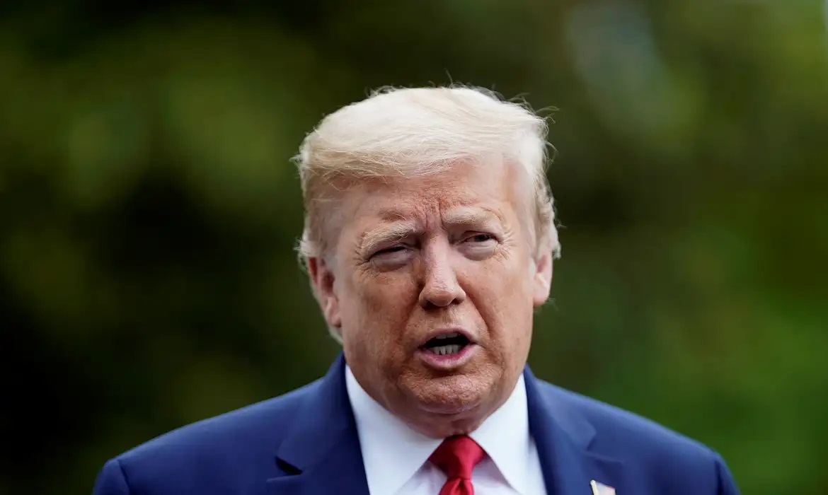O presidente Donald Trump falando, sério, de terno e gravata