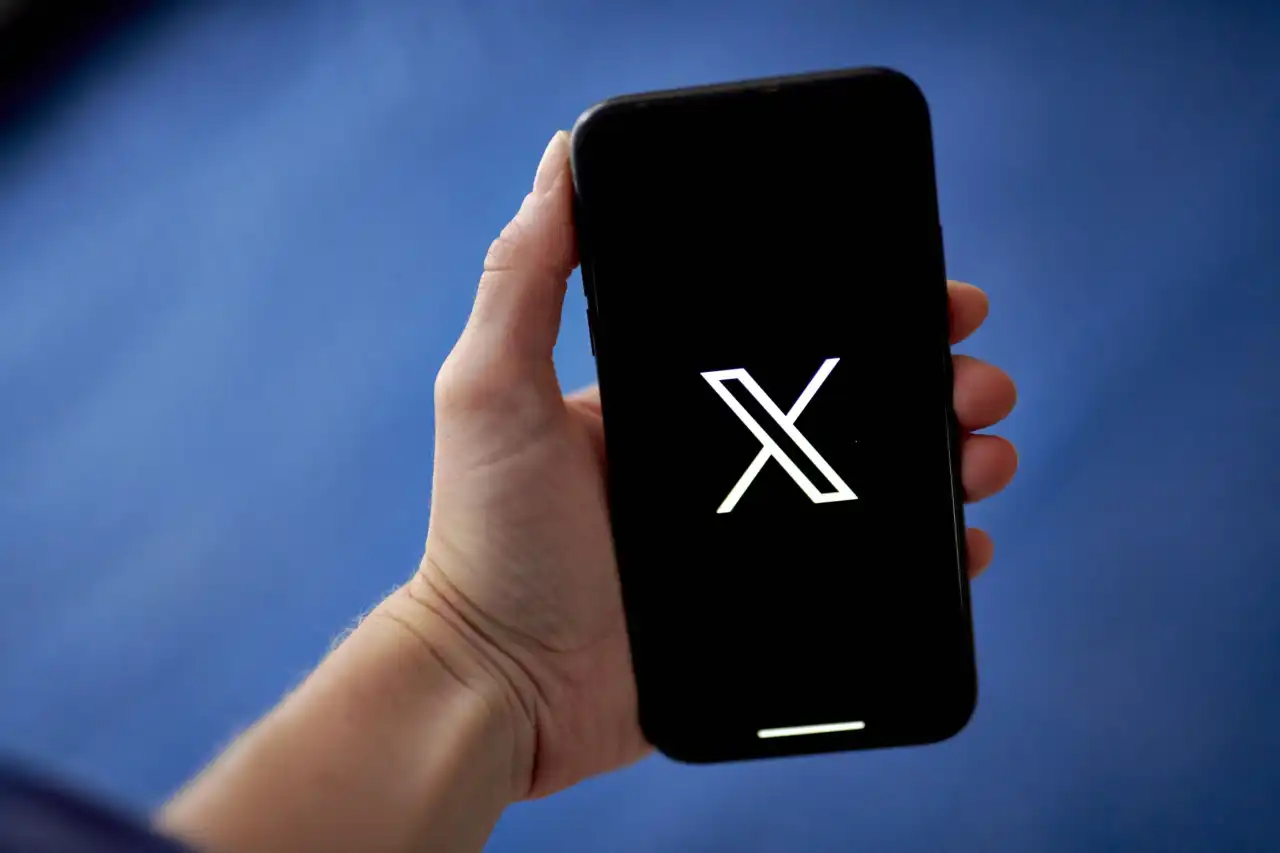 Mão segurando celular com a logo do X no fundo