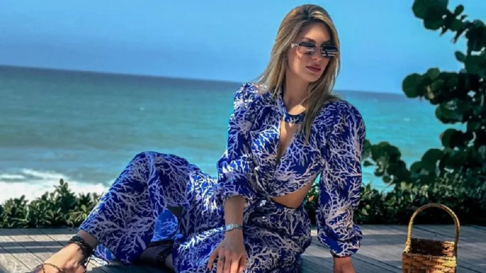 A modelo Shara Fornalevicz Soares posando de roupa azul e óculos escuros perto do mar