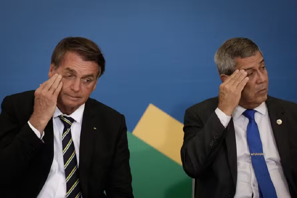 Jair Bolsonaro e Walter Souza Braga Netto cabisbaixos e com as mãos no rosto