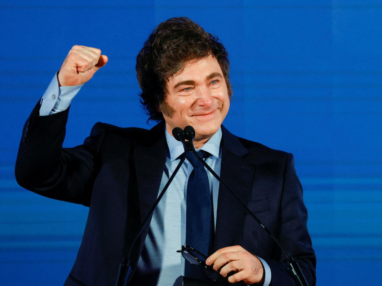 Javier Milei, presidente da Argentina, de terno e gravata, comemorando com um braço levantado