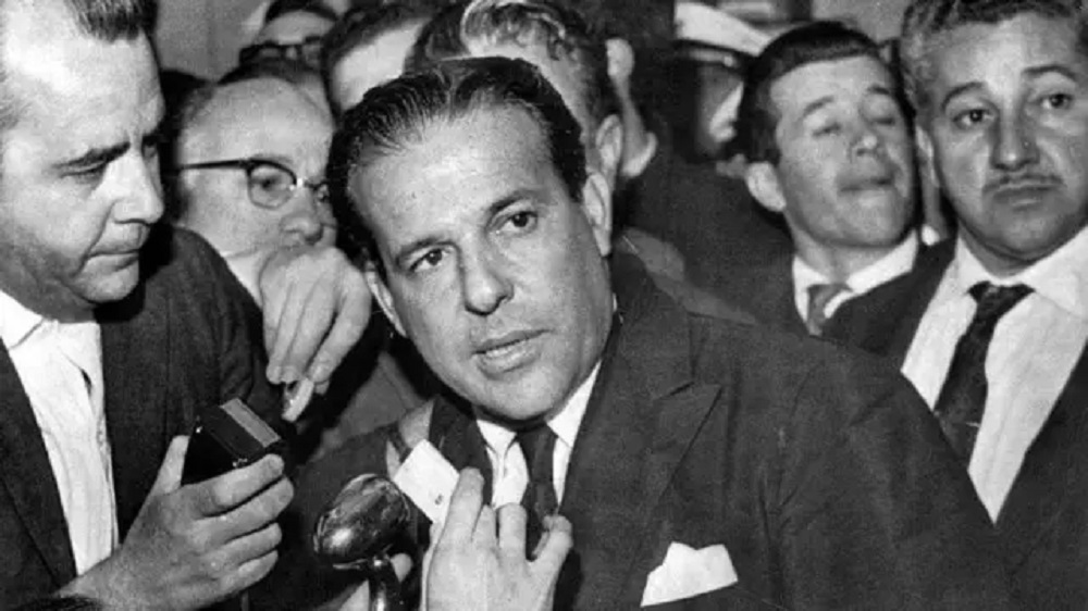 João Goulart, em foto em preto e branco, sério, olhando para o lado, rodeado de pessoas, de terno e gravata