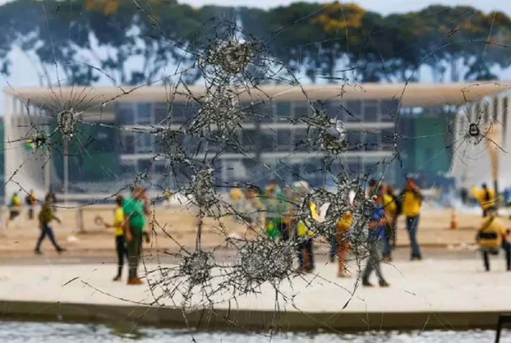 Golpistas em Brasília em 8 de janeiro de 2023, vistos através de vidro quebrado
