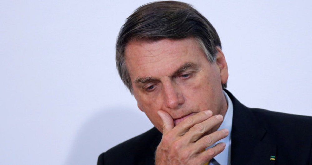 Jair Bolsonaro cabisbaixo passando a mão na boca