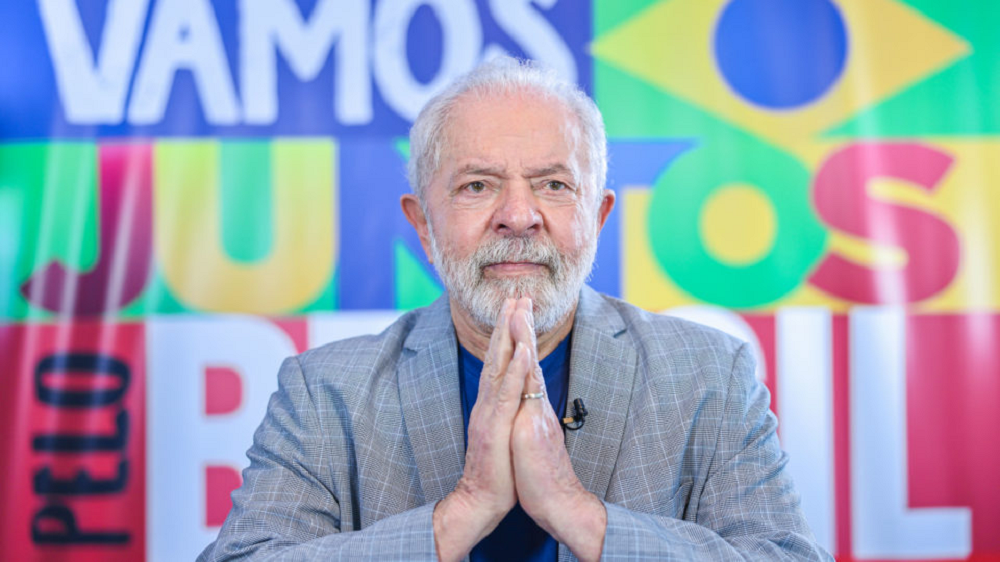 Luiz Inácio Lula da Silva (PT) com mãos unidas em sinal de agradecimento e expressão tranquila, sem olhar para a câmera