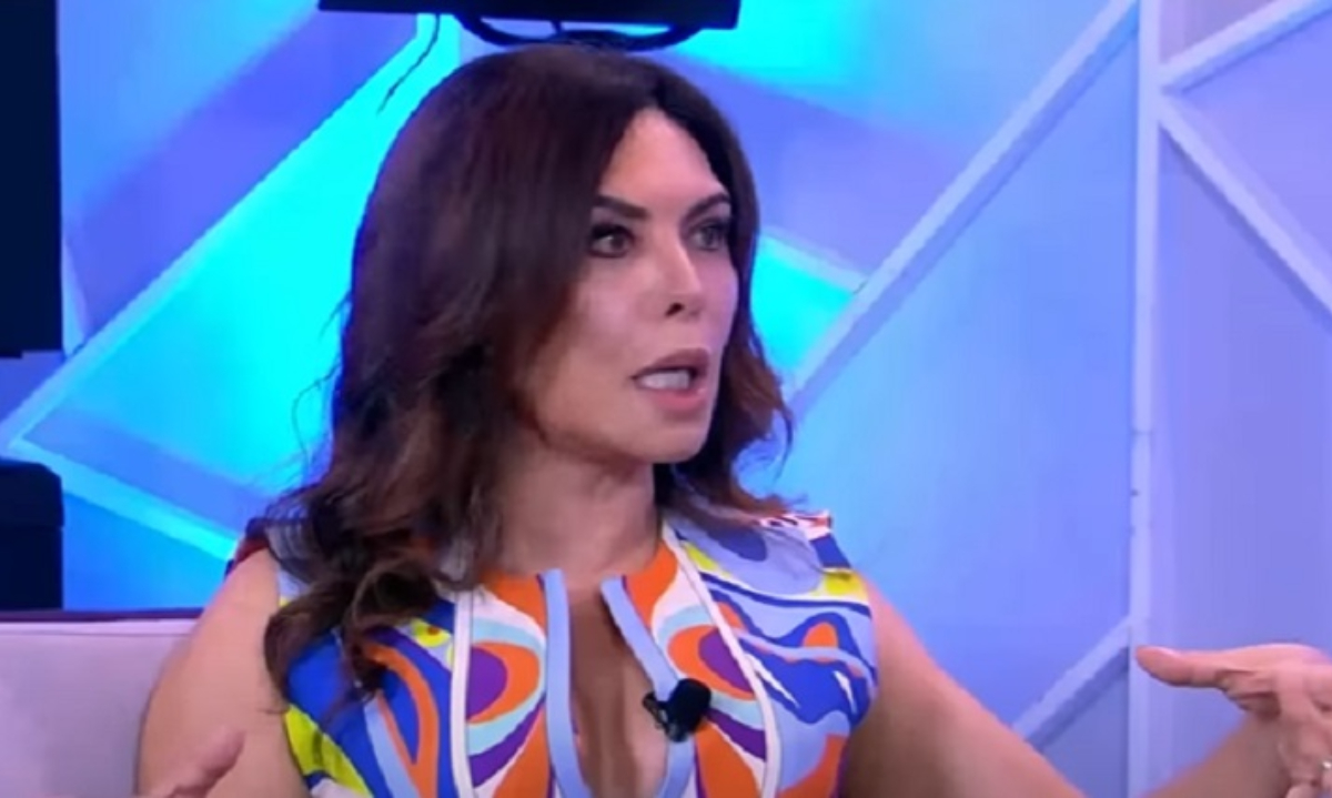 Márcia Goldschmidt falando e gesticulando, séria, sem olhar para a câmera, de roupa estampada e cabelo solto