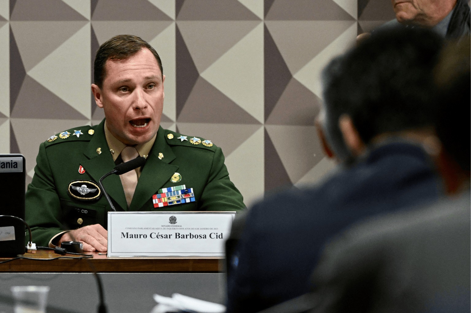 O tenente-coronel Mauro Cid no fundo de foto, fardado, falando