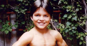 Richard Sandrak ainda criança, sem camisa, de sunga azul, sorrindo para a câmera