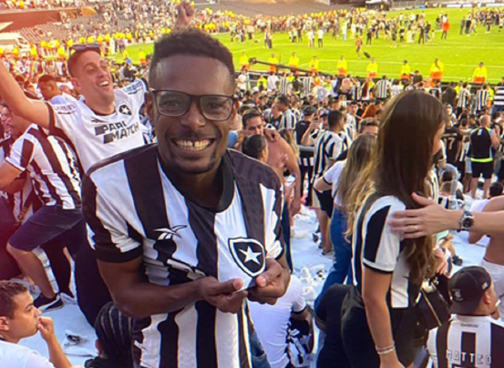 Igor de Melo em estádio, sorrindo e mostrando blusa do Botafogo