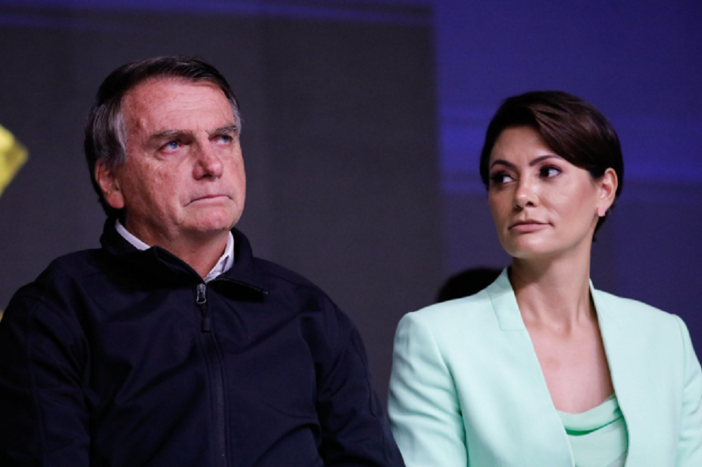 Jair Bolsonaro (PL) e Michelle Bolsonaro sentados lado a lado, sérios, ela olhando pra ele
