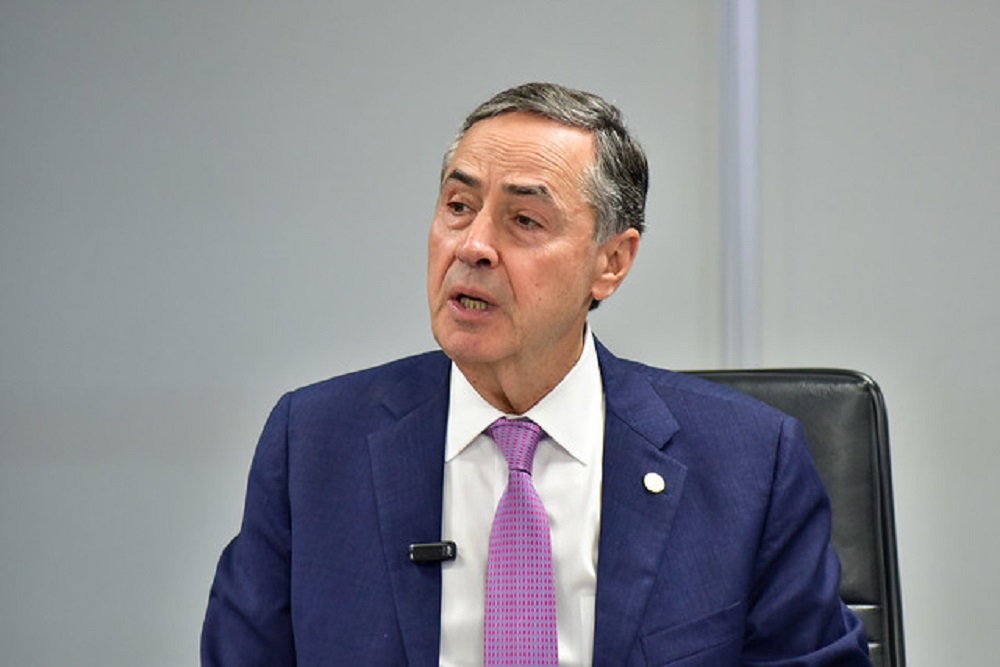 O ministro Luís Roberto Barroso falando e olhando para o lado, sério, de terno e gravata
