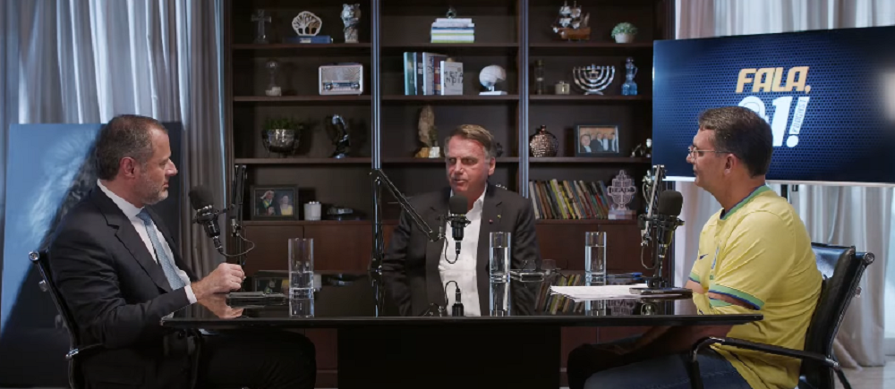 Paulo Amador da Cunha Bueno, Jair Bolsonaro e Flávio Bolsonaro sentados à mesa e falando