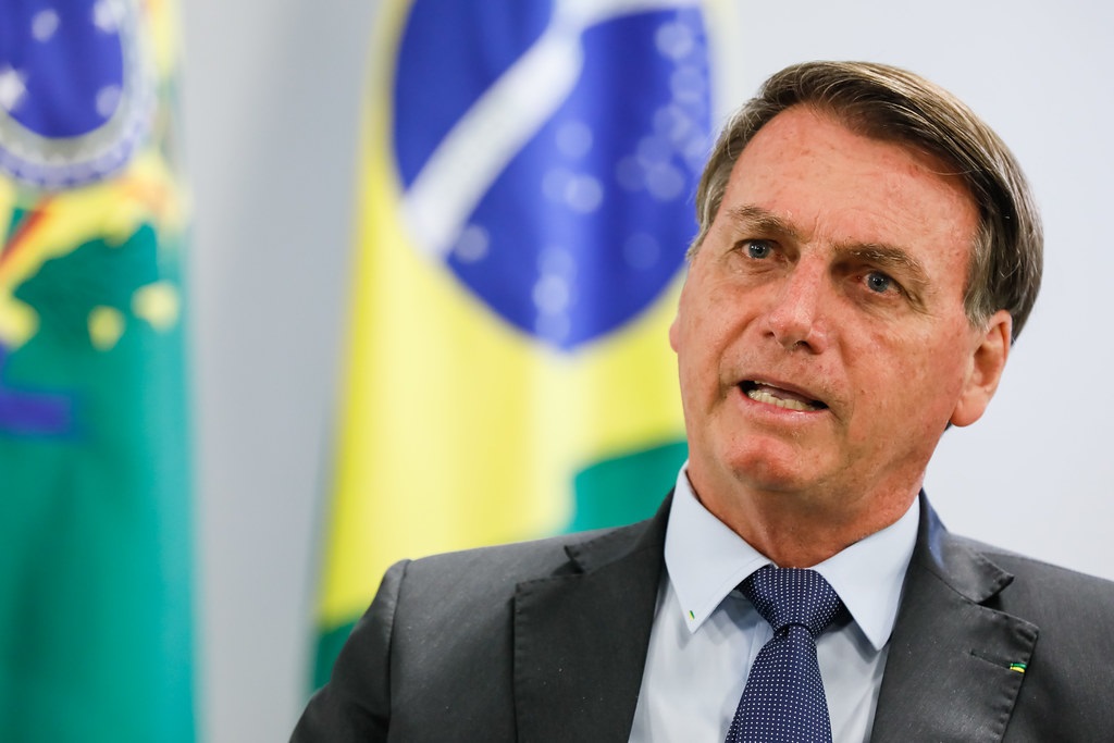 O ex-presidente Jair Bolsonaro (PL) falando, sem olhar para a câmera, com bandeiras ao fundo