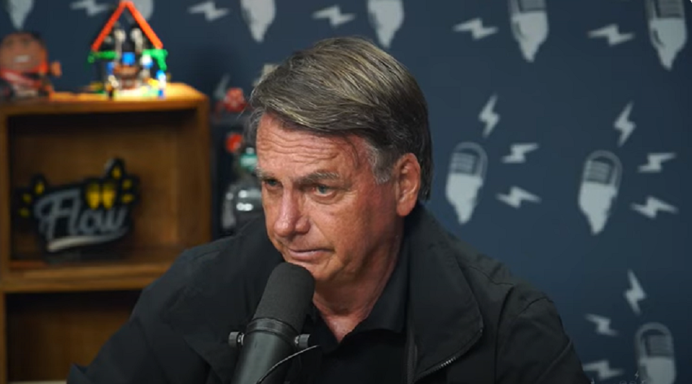ex-presidente Jair Bolsonaro (PL) sério, sem olhar para a câmera, de roupa de frio preta, perto de microfone, no Flow