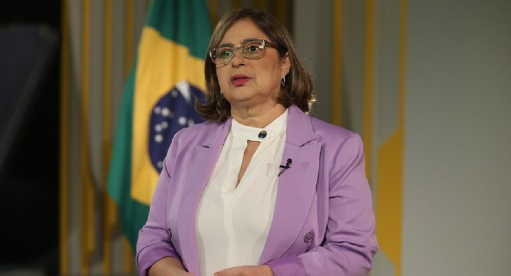 ministra das Mulheres, Cida Gonçalves, de roupa lilás e branca, de óculos e cabelo solto, falando e gesticulando sem olhar para a câmera