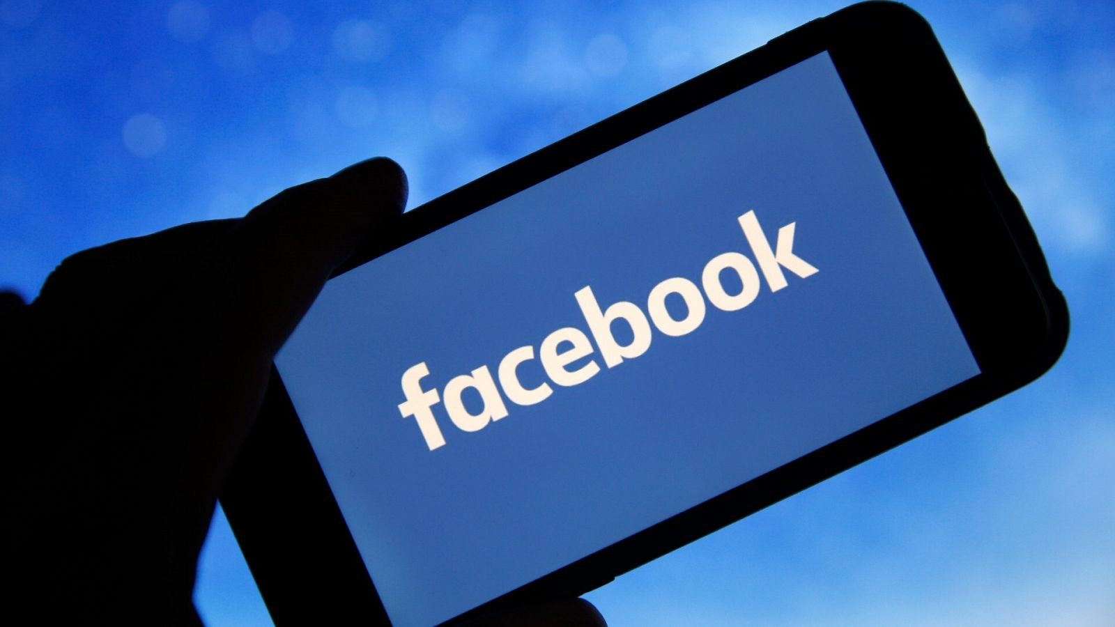 Mão segurando celular com logo do Facebook na tela