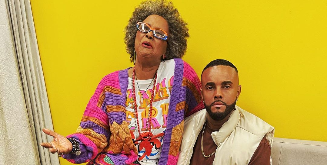 A cantora Sandra Sá e o ator e empresário Jorge de Sá posando para foto sentados, ela falando e ele sério, em fundo amarelo