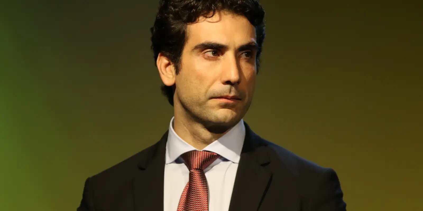 Gabriel Galípolo olhando para o lado, sério, de terno e gravata