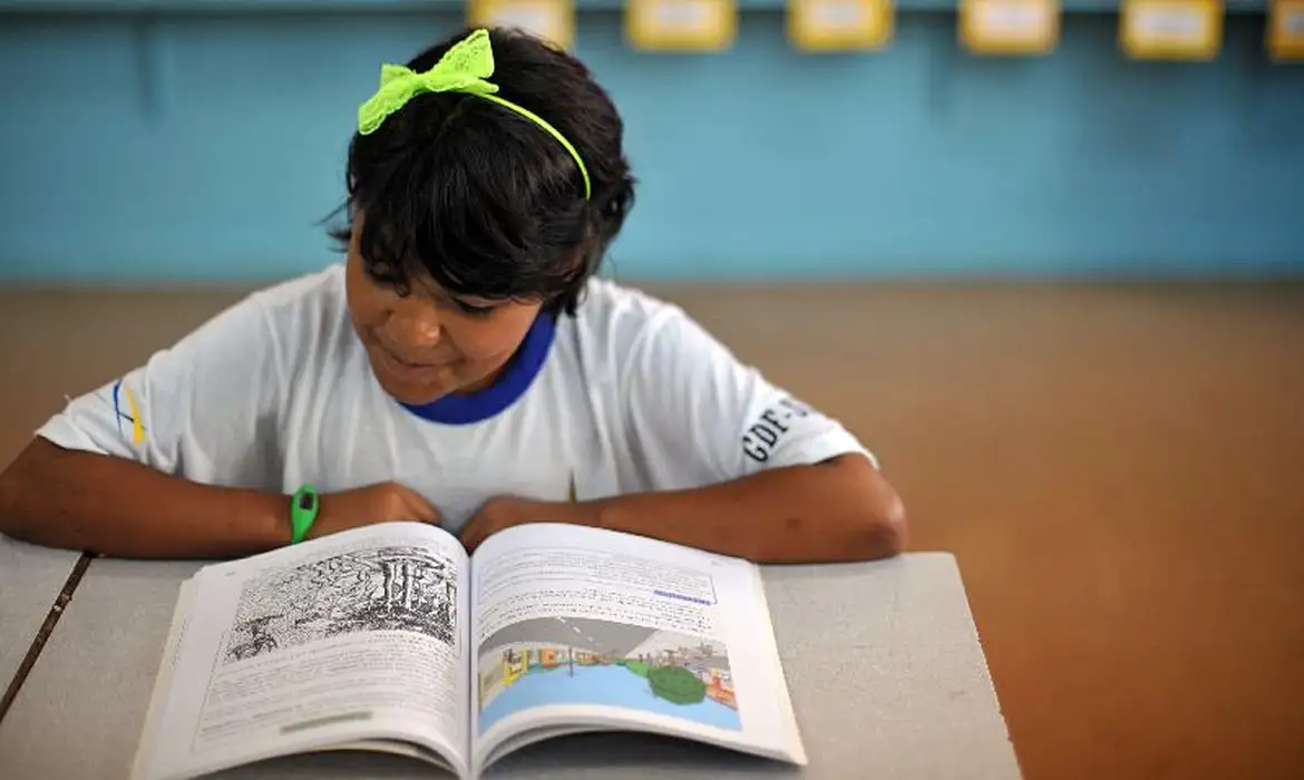 Menina lendo livro de cabeça baixa em sala de aula